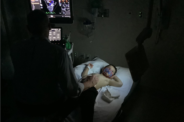 Boy lay on bed with echocardiogram images shown on a monitor next to him