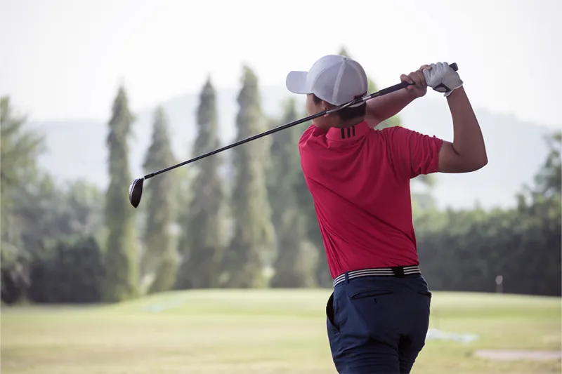 Golfer wearing hat follows through on their swing