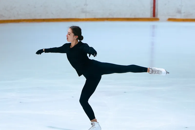 Woman skates across the ice while holding right leg up in air