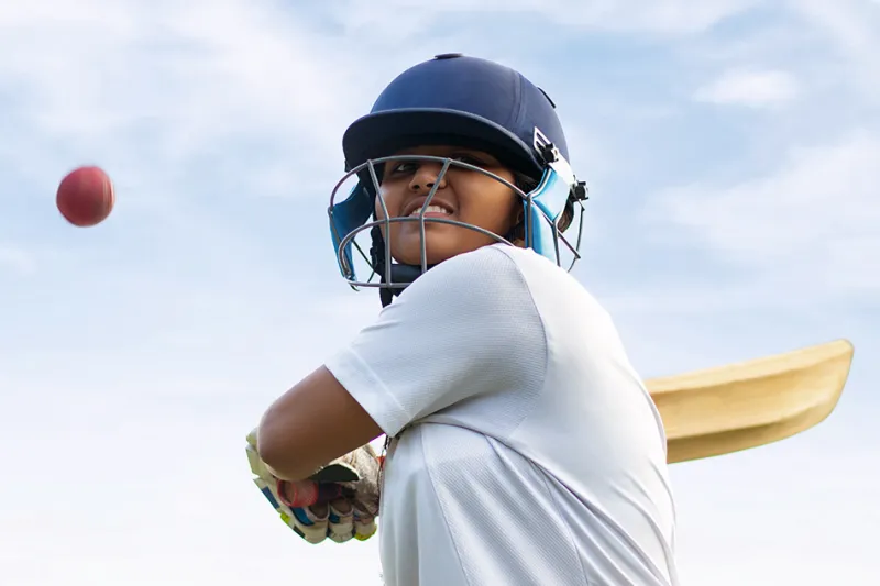 Cricket player wearing helmet and holding bat prepares to swing at ball in the air