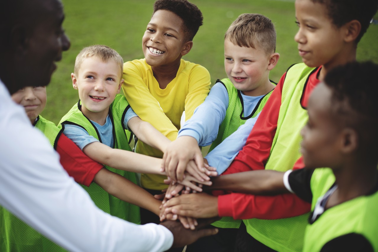 kids playing soccer with hands in a circle and smiling