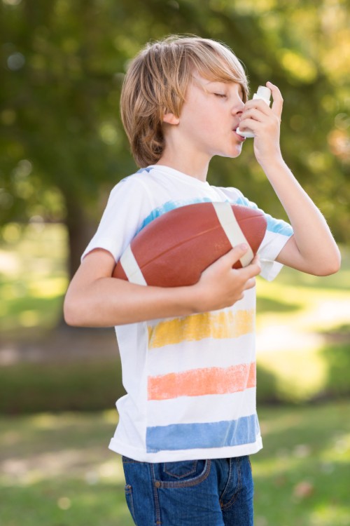 Child holds football and uses inhaler