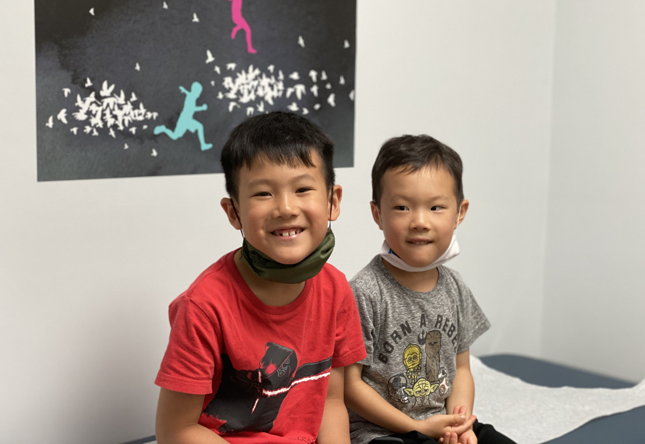 Two boys sit, smiling, in a doctor's office