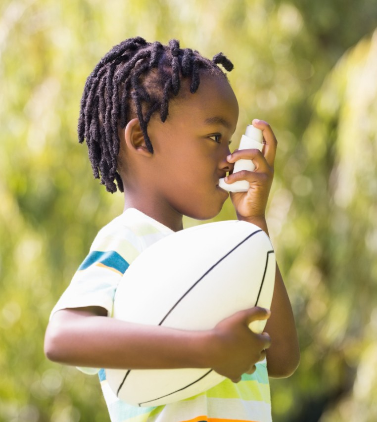 Child bolds inhaler in left hand and football in right hand