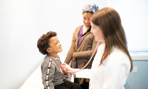 a smiling young boy as a pediatrician listens to his heartbeat