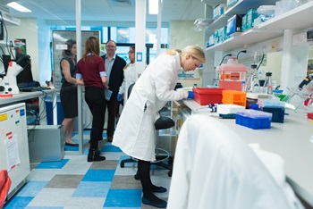 A woman leans over a lab table while a group of people talk together behind her.