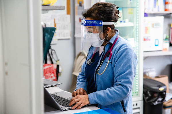 a doctor with ppe looking at a laptop