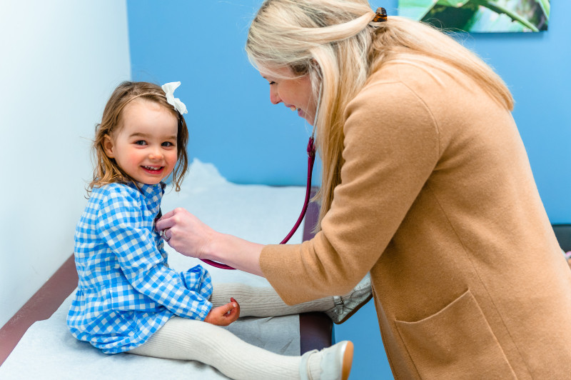 girl smiling as a pediatrician listens to her heart