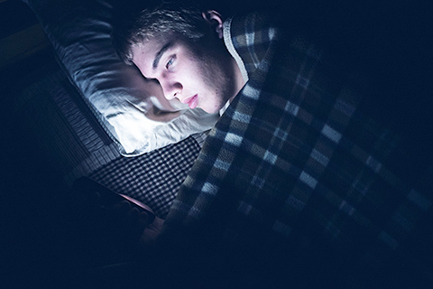 Boy looks at smartphone while under the covers and in bed