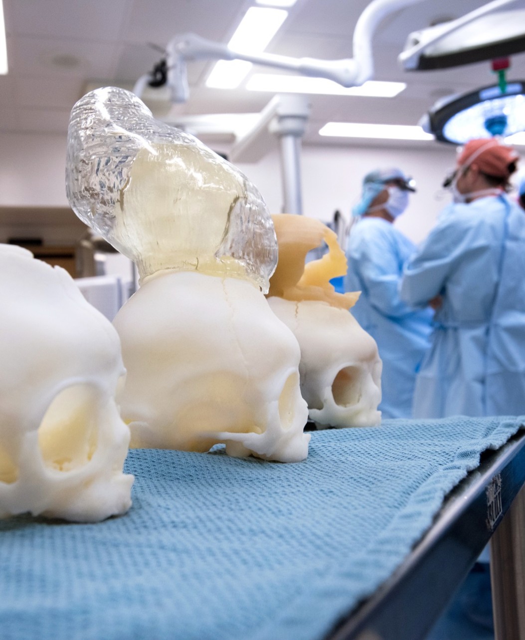 Three simulation skulls sit on a table in front of doctors in scrubs who are looking away from the camera.