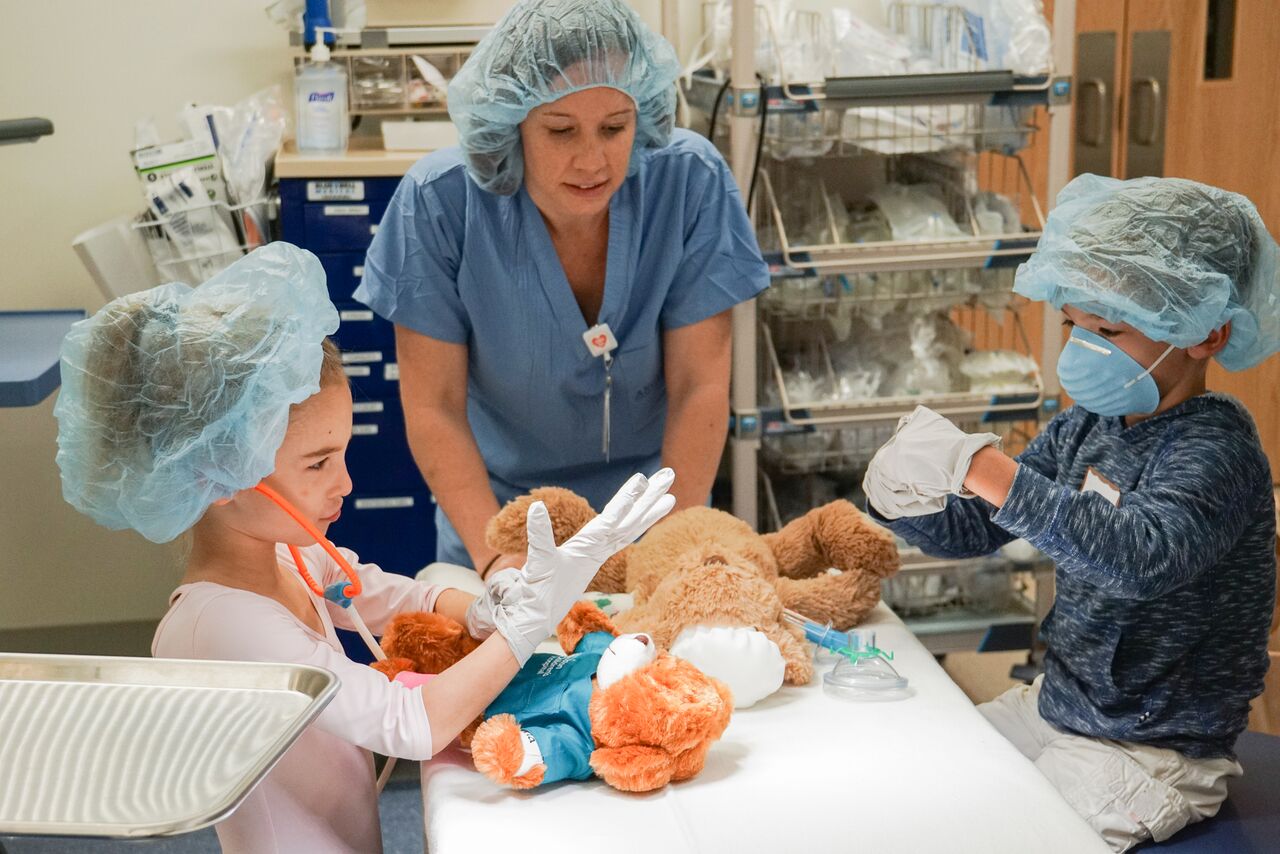 Two children and a doctor work on teddy bears. 