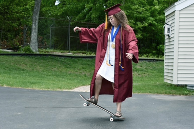 Girl wearing graduation cap and gown plays on skateboard