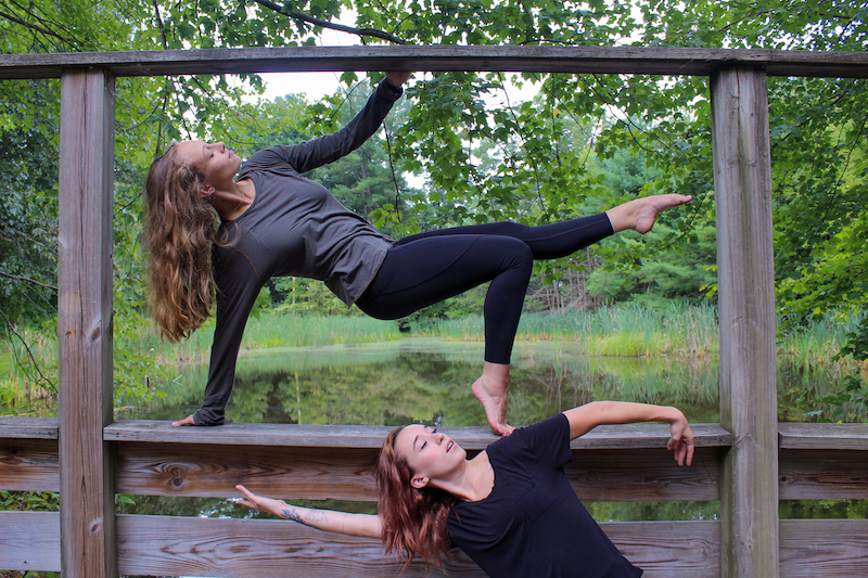 Two teen girls perform dance moves outdoors in a wooded area