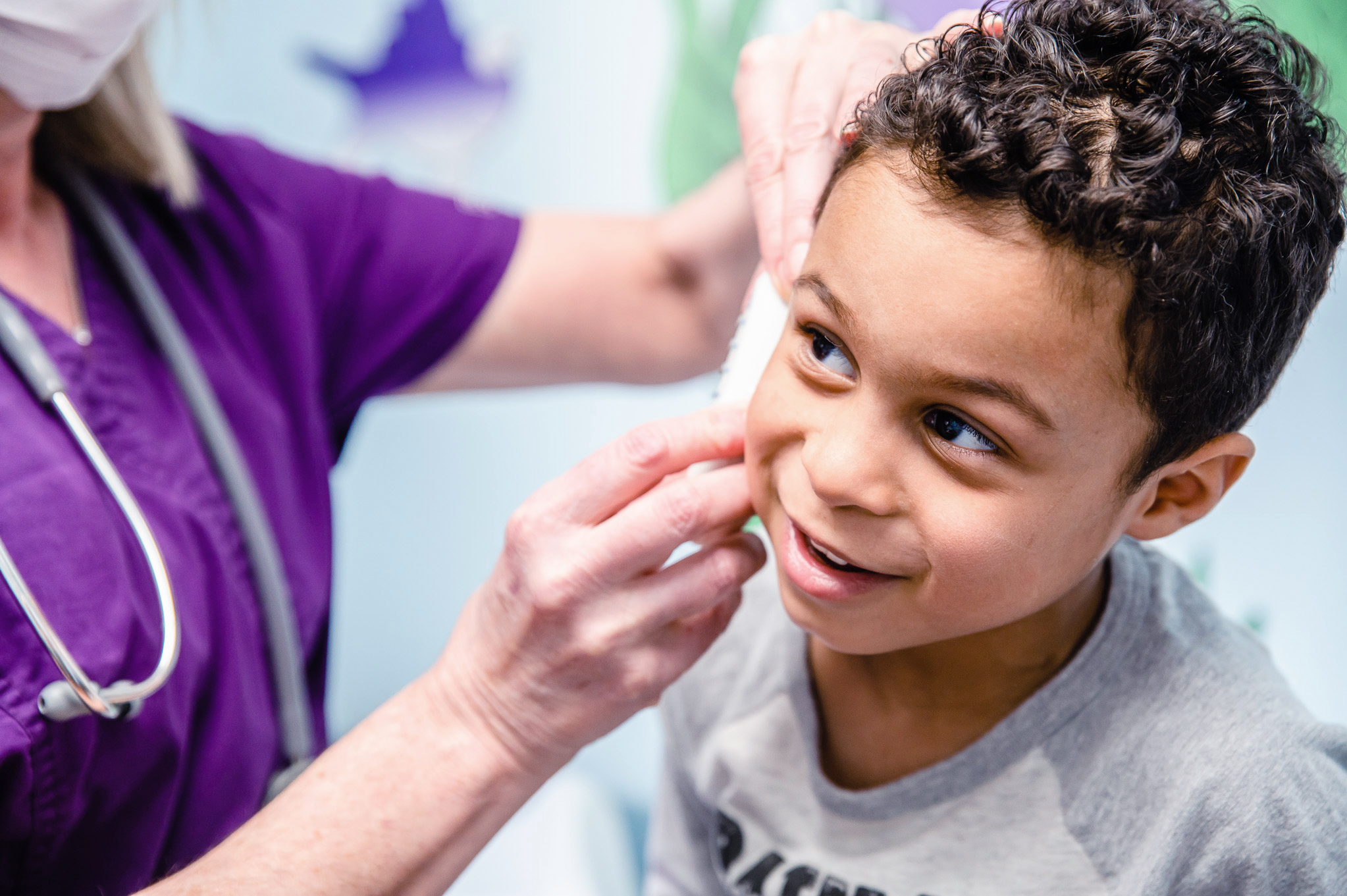 young boy smiling while getting his ear examined