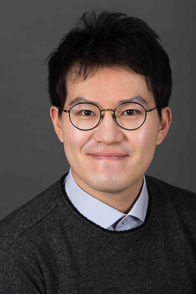 Headshot of Hyunyong Koh, an asian man wearing round glasses stares at the camera with a closed-lip smile.