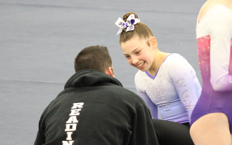 Mikayla talks to a coach and smiles after competing in a gymnastics event.