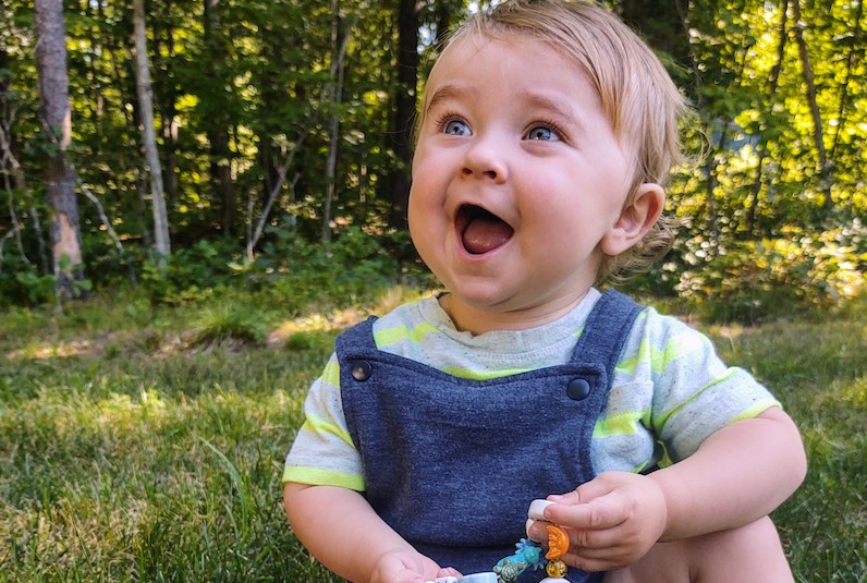 Blonde toddler with a big smile while outside.