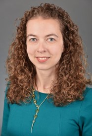 Headshot of Anne O'Donnell Luria, a woman with curly red hair wears a teal shirt and a necklace.