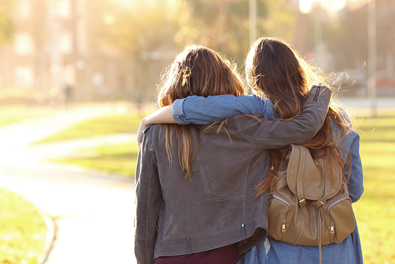 Two teens hold arms around each other while walking down a pathway.