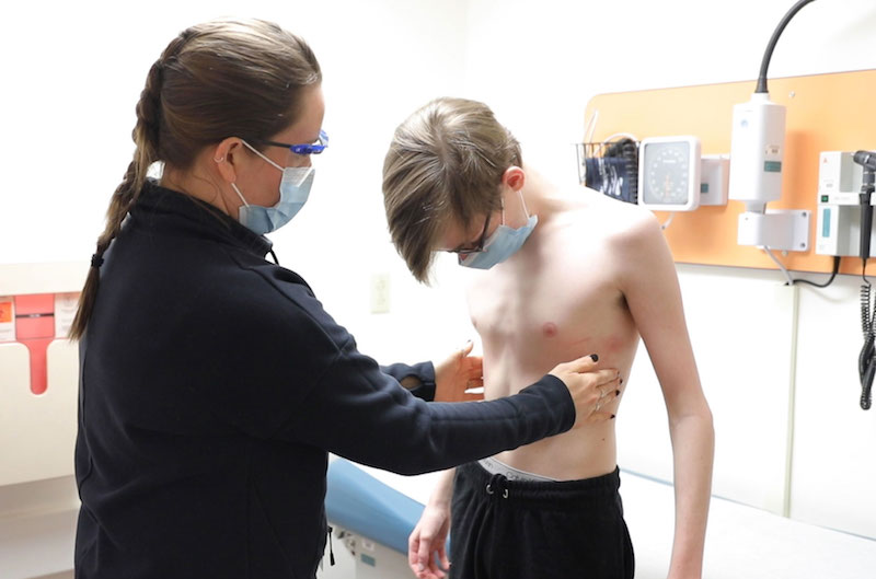 A woman doctor measures a young boy's chest wall.
