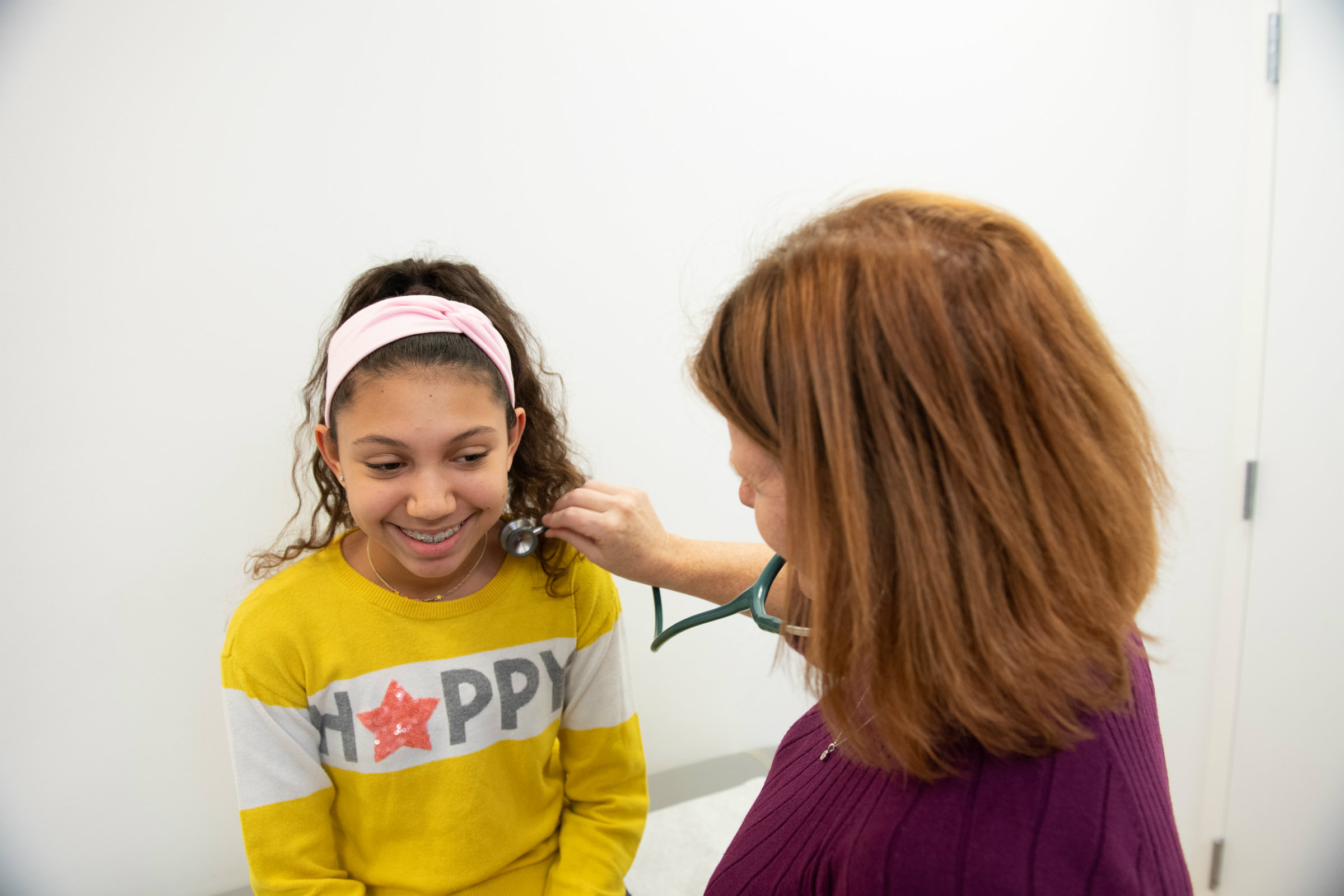 a doctor holding a stethoscope to a girl's neck