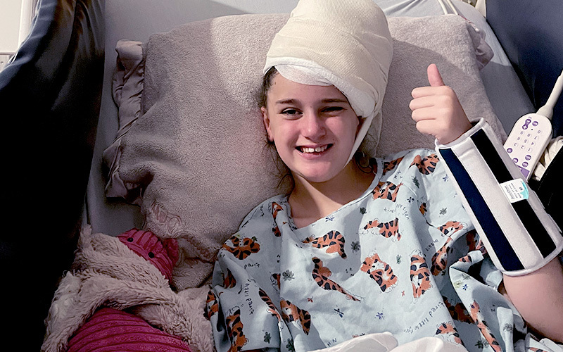 Girl lay in bed and gives thumbs up sign.