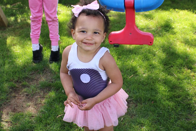Little girl outside, smiling at camera in pink tutu