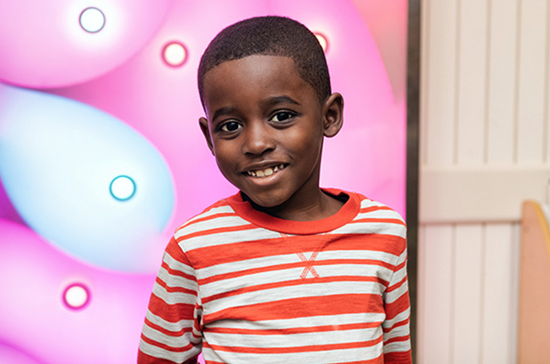 Smiling young boy stands in front of wall painted pink and sky blue