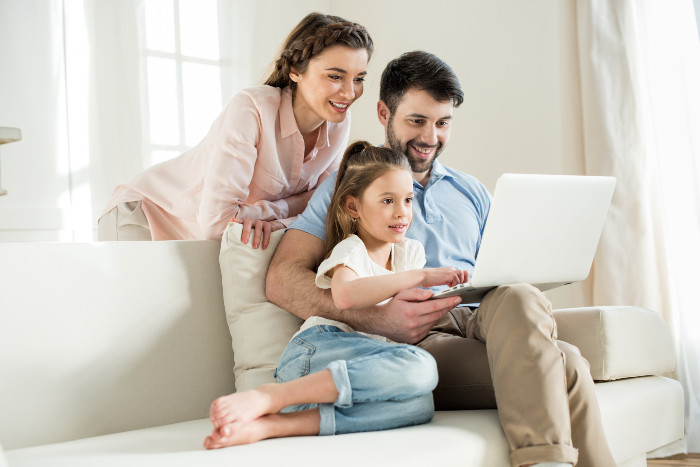 a mother, father and daughter looking at a laptop
