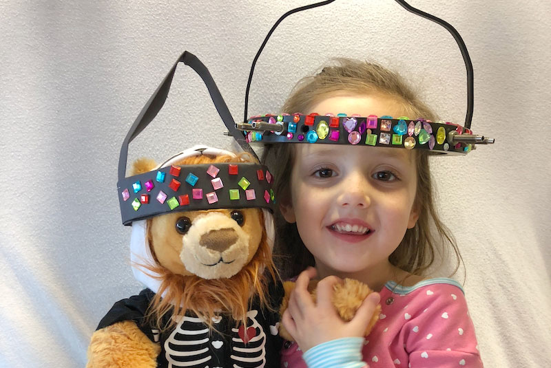 Gracie holds a teddy bear also wearing a halo like she is.