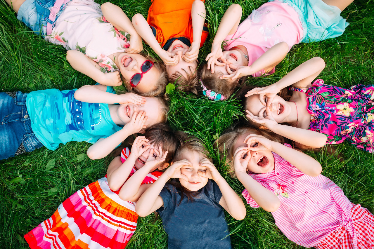 a ring of kids lying on the grass looking up through their hands