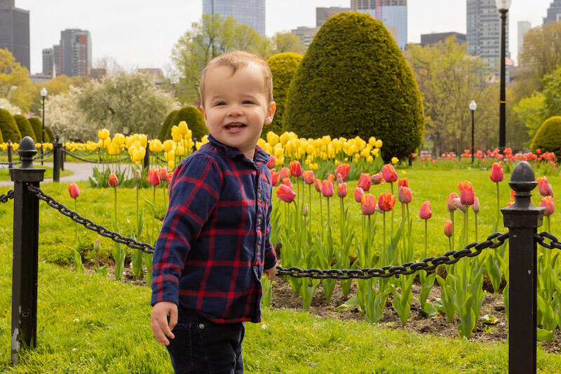 Micah smiles while standing in a garden with the Boston skyline behind him.