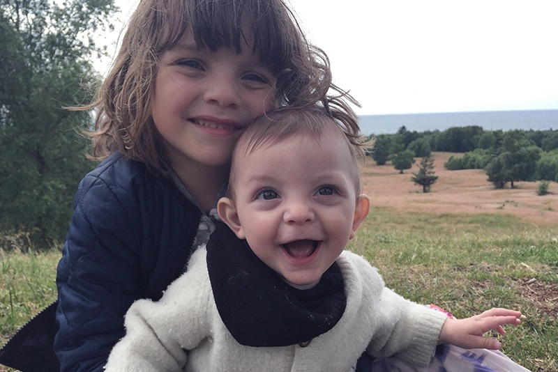 Toddler boy and young girl smile while posing in a farm field.