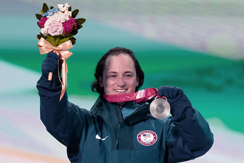 Paralympian holds silver medal and bouquet of flowers after competition.