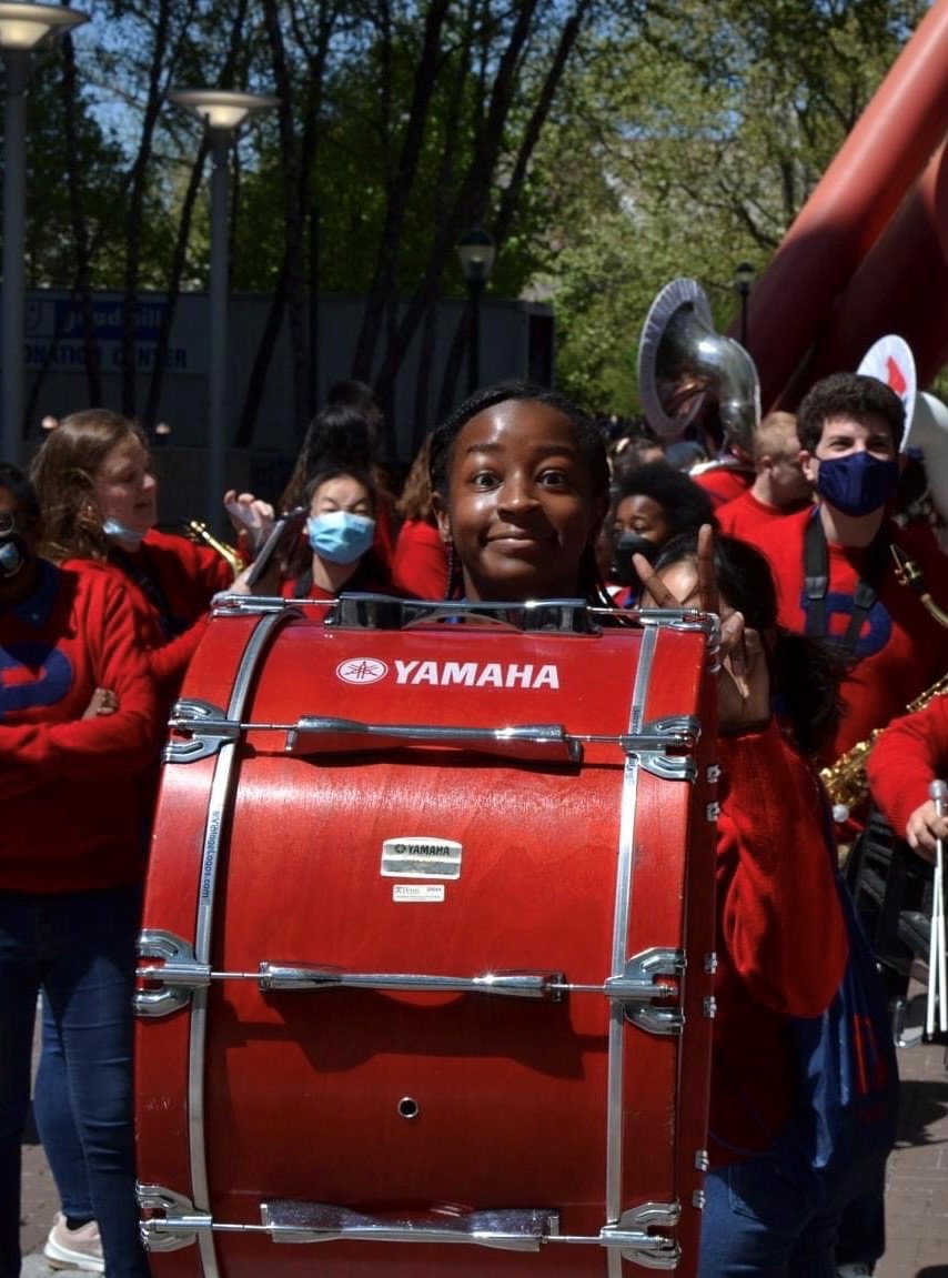 A student stands behind a red yamaha drum in a school marching band parade.