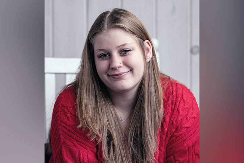 Smiling teenage girl with blonde hair and red sweater poses for the camera