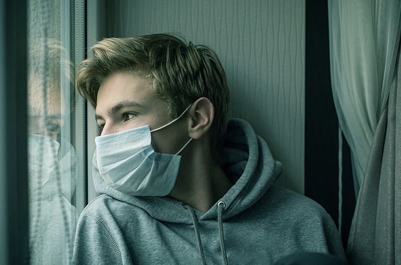 Teenager wearing a medical grade disposable face mask stares out a window