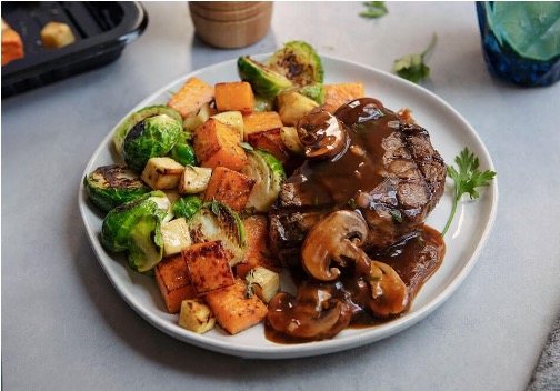A healthy meal of steak with a mushroom sauce and carrots and brussel spouts on the side. 