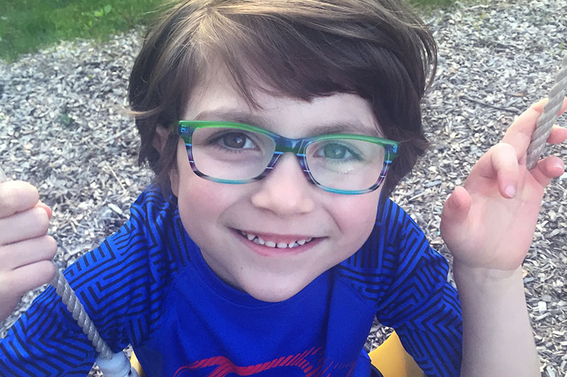 Boy wearing glasses and sitting on swing looks up at camera