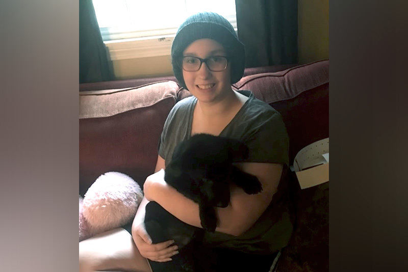 Teenage girl sits down while holding her cat.