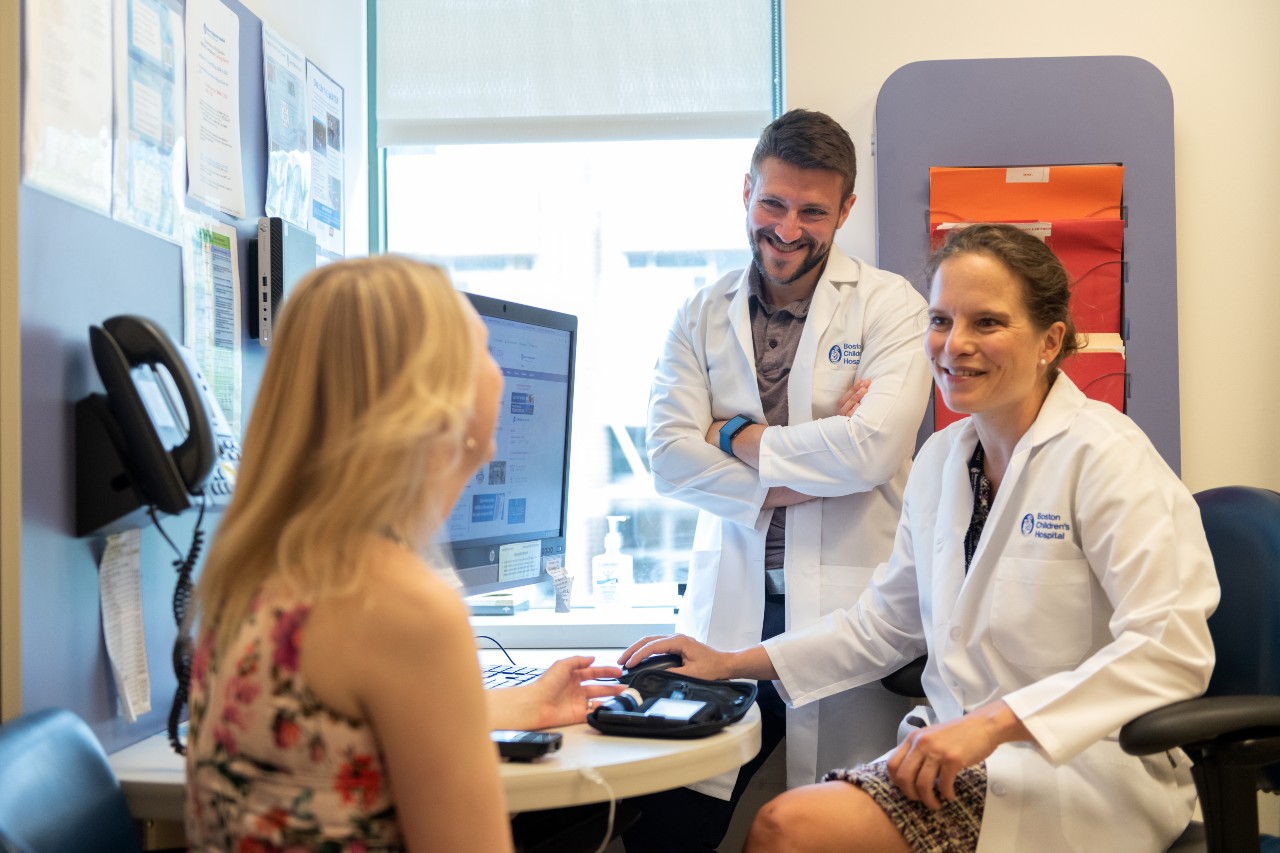 Two doctors sit across a small round table from a blonde woman.