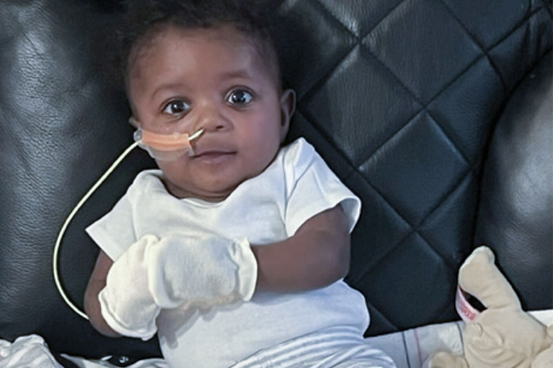 Baby sits on chair and stares directly into the camera.