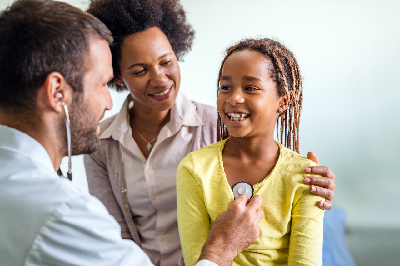 a doctor using a stethoscope to listen to a girl's chest while her mom supports her