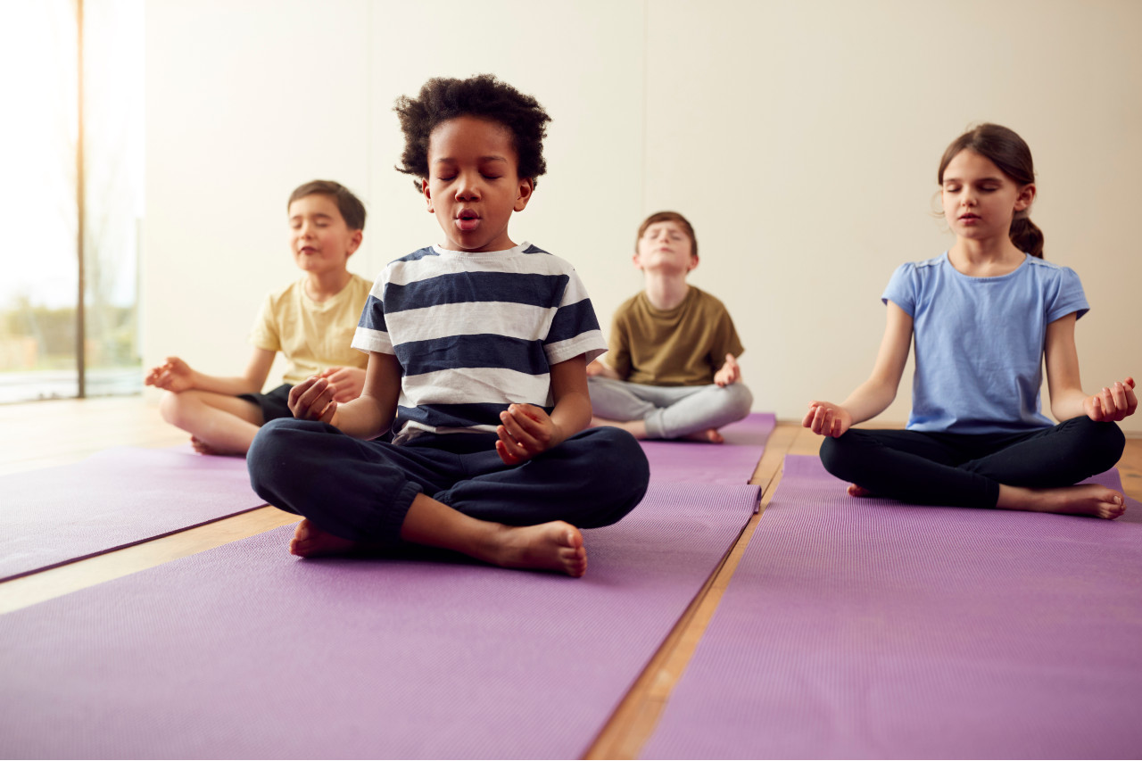 four childrens sitting crossleg on yoga mats with their eyes closed