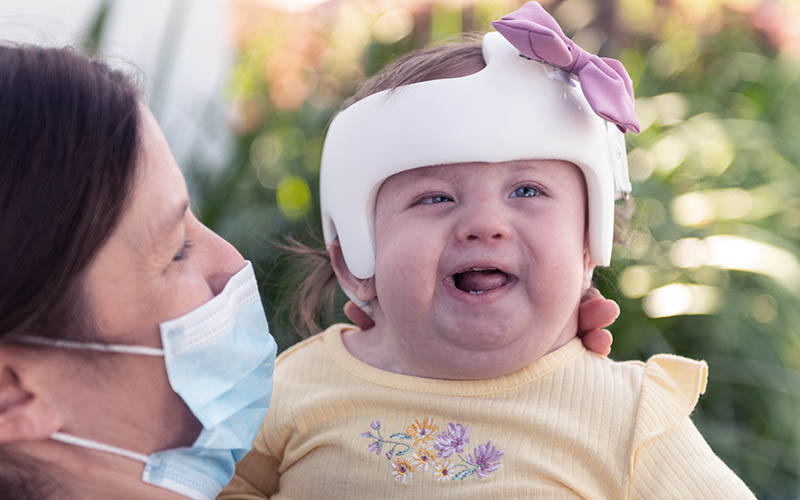 Mom wearing face mask holds daughter wearing yellow shirt