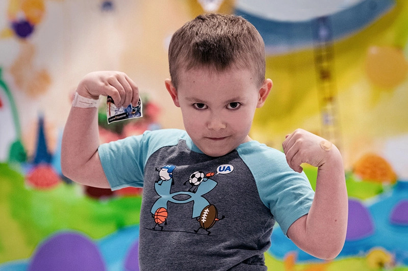 Young boy flexes his muscles while wearing a blue and gray T-shirt