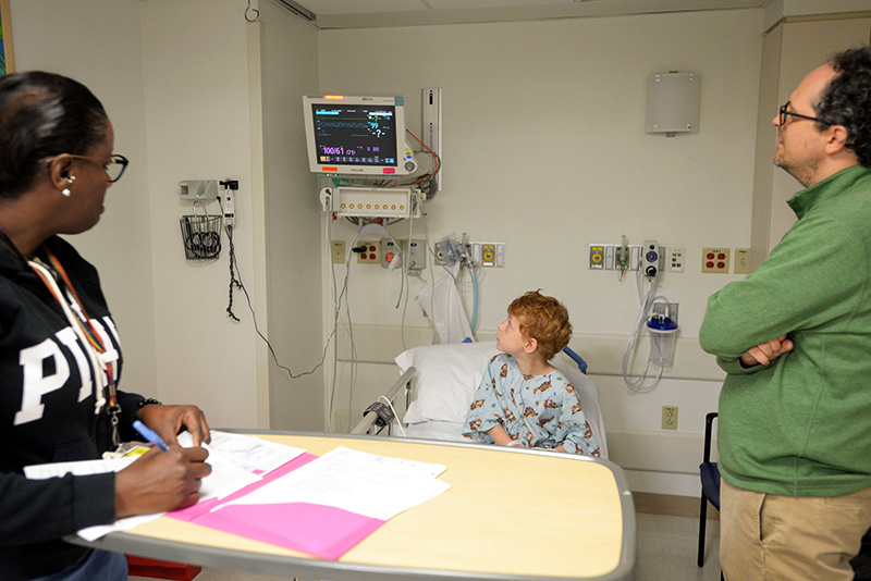 Boy, parent, and clinician look at monitor in hospital room
