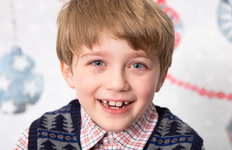 Young boy with brown hair smiles in front of camera