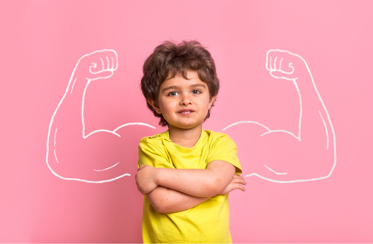 a child crossing his arms in front of a pink background with an outline of muscular arms around him