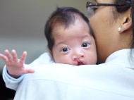 A doctor holds a baby with a cleft lip palate as they stretch an arm out.